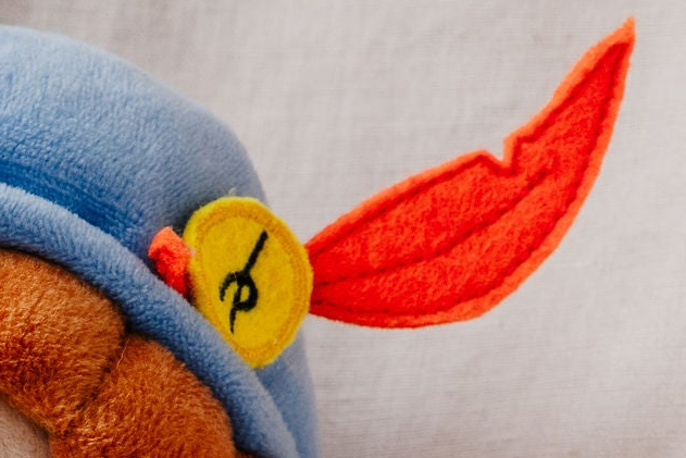 Close-up van de blauwe muts van de Piet die 't Ziet-knuffel met rode veer en geel embleem met P-handtekening