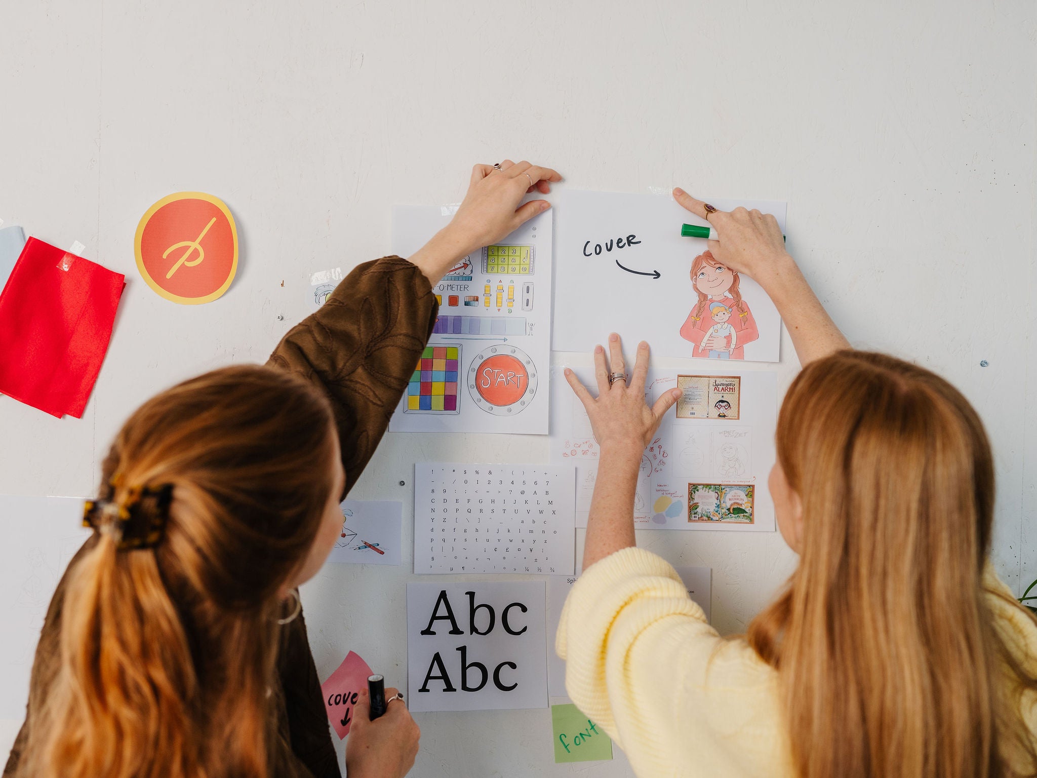 Twee makers hangen conceptillustraties en coverontwerpen van De Piet die 't Ziet op aan een moodboardmuur