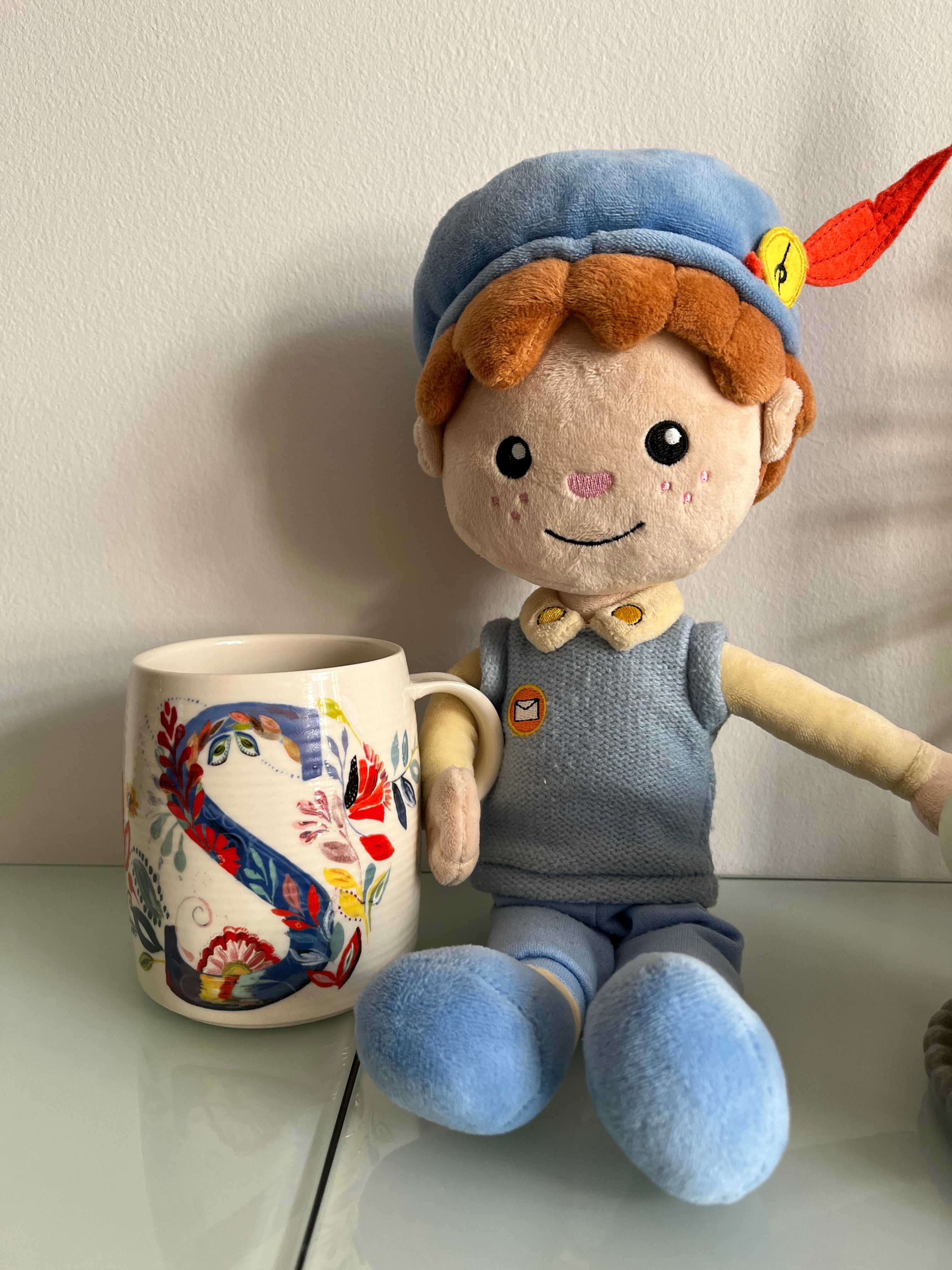 De Piet die 't Ziet-knuffel zit naast een beschilderde mok met de letter S op een glazen tafel