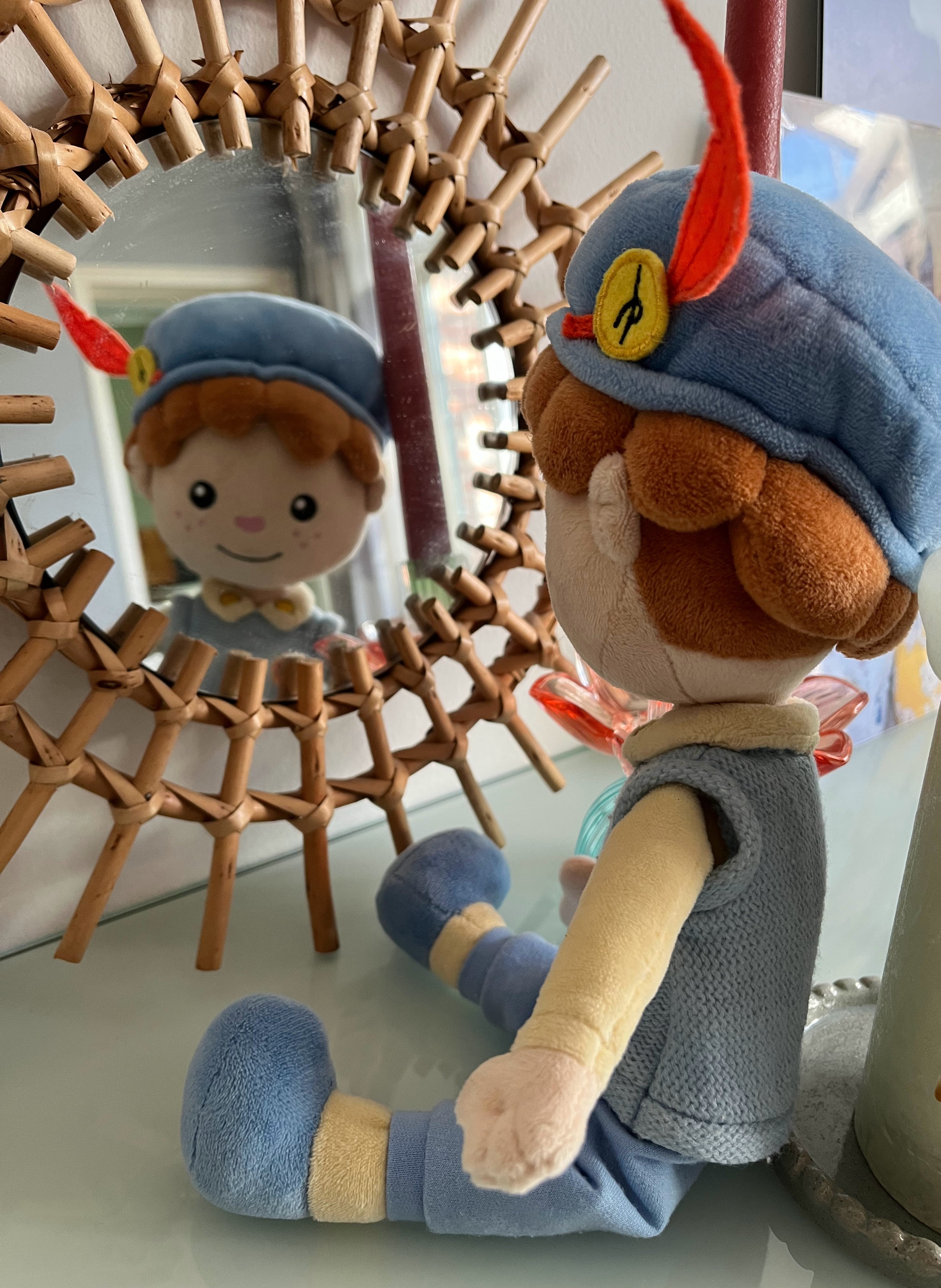 De Piet die 't Ziet-knuffel zit voor een rieten spiegel, waarin zijn spiegelbeeld te zien is