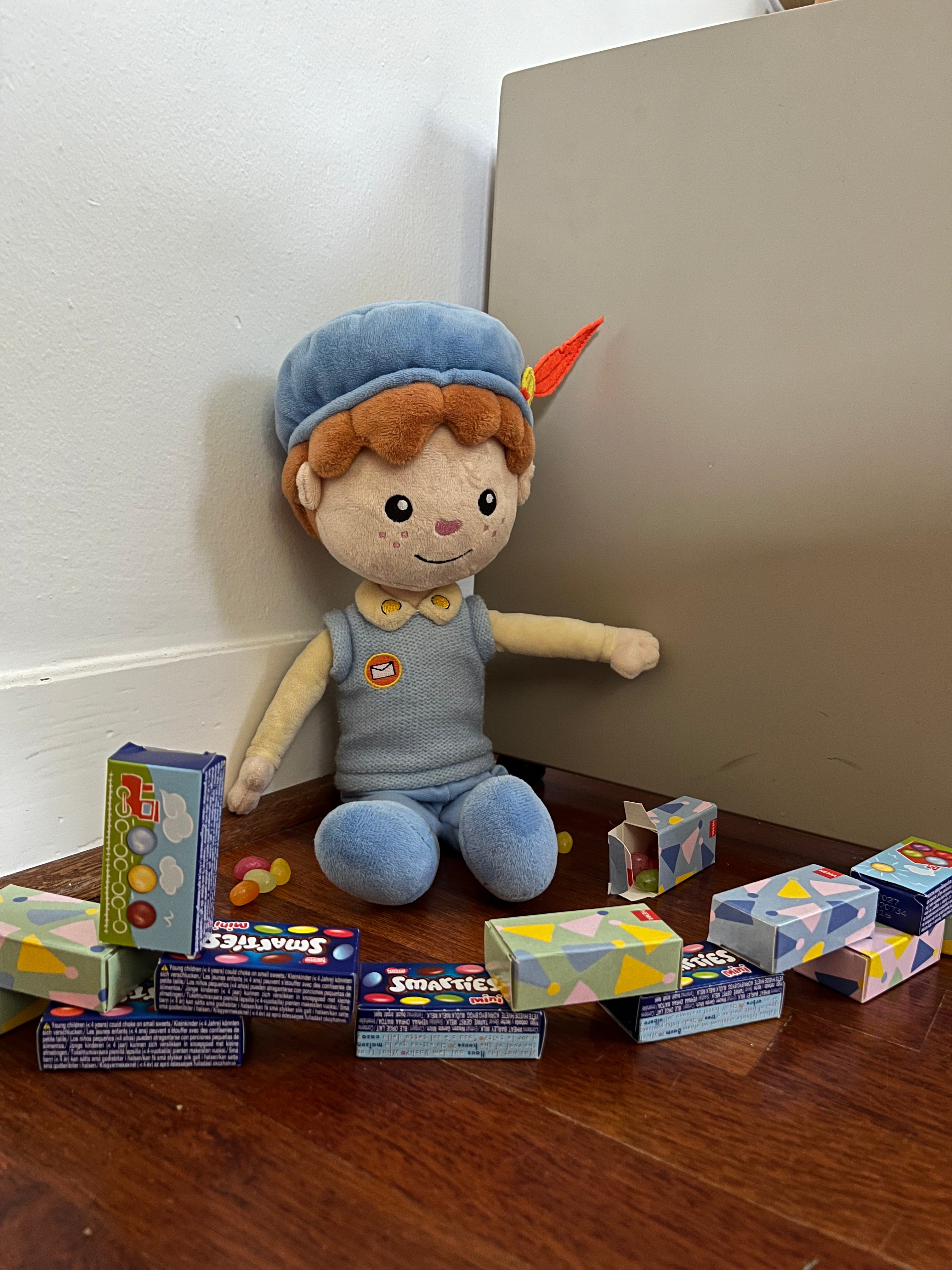 De Piet die 't Ziet-knuffel zit tussen een verzameling Smarties-doosjes op de houten vloer